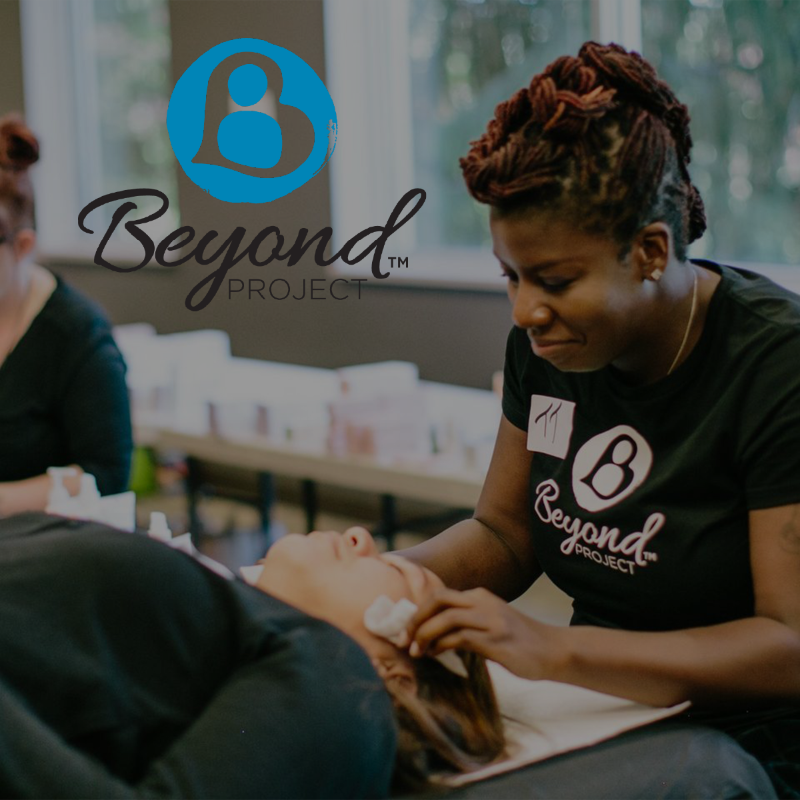 Blue circular logo with "Beyond Project" text over woman providing facial service on client.